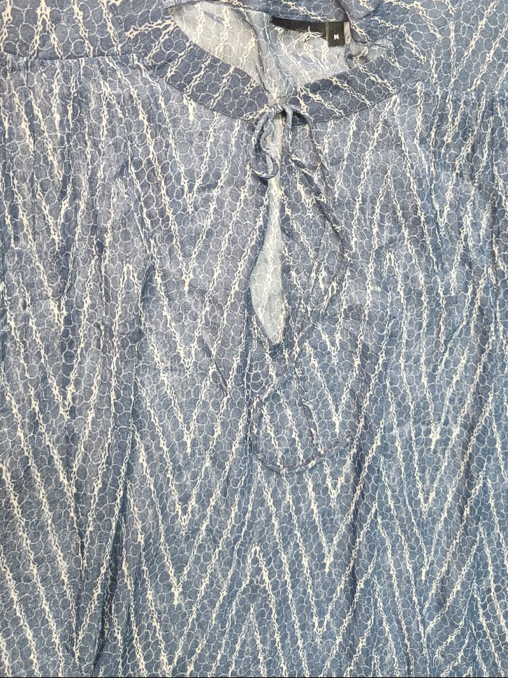 A close-up of a blue and white patterned blouse with a tie-neck detail, laid flat against a white background.