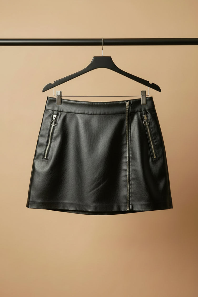 A black faux-leather mini skirt with two silver zipper details on the sides, hanging on a wooden hanger against a light beige fabric background.