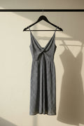 A sleeveless V-neck dress with a small white floral print on a navy blue background, hanging on a wooden hanger against a white fabric backdrop.