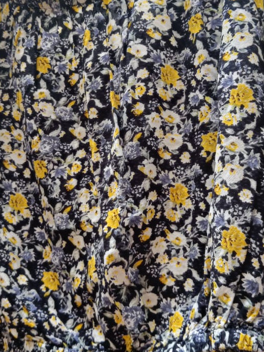 A long-sleeve blouse with a dense floral print, hanging on a wooden hanger from a tree branch in an outdoor setting.