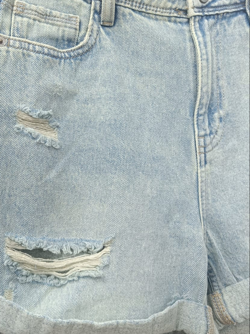Light wash distressed denim shorts with rolled hems and frayed rips, hanging on a black hanger against a red background.