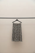 A black and white patterned midi skirt hanging from a wooden clothes hanger on a tree branch in an outdoor patio setting.