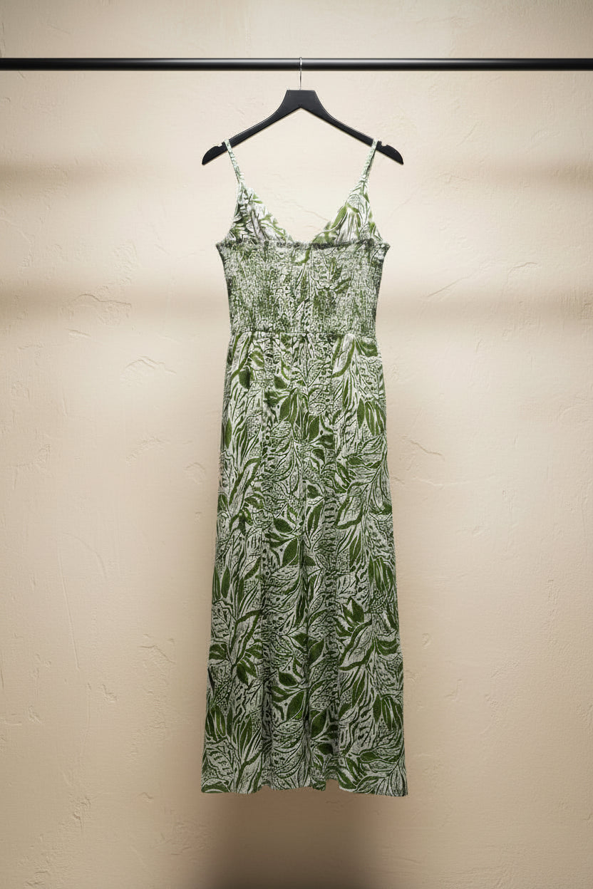 A sleeveless maxi dress with thin spaghetti straps, featuring a green and beige botanical leaf pattern, laid flat on a white fabric background.
