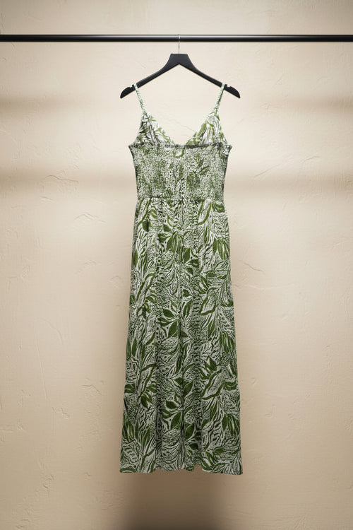 A sleeveless maxi dress with thin spaghetti straps, featuring a green and beige botanical leaf pattern, laid flat on a white fabric background.