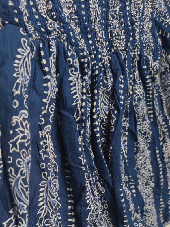 A close-up of a blue fabric garment with white floral and dotted vertical patterns, showing gathered texture and folds against a plain light background.