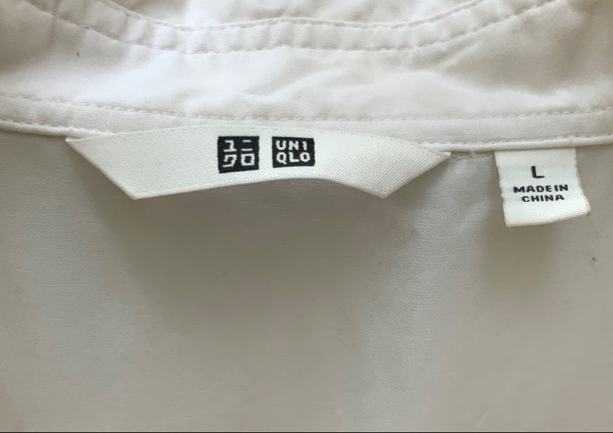 Close-up of a white Uniqlo blouse hanging on a light wood hanger, showing the inner neck label with the Uniqlo logo and a size tag marked L.