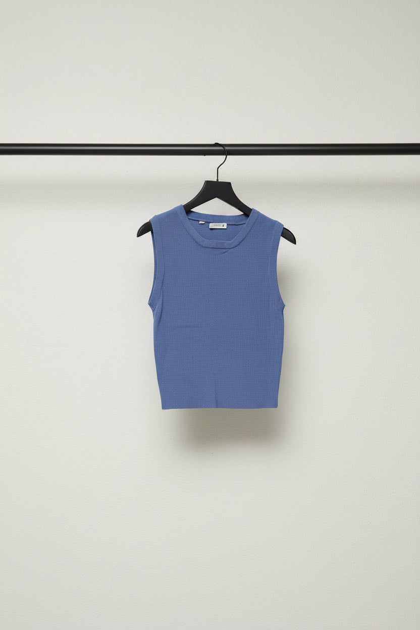 A sleeveless, ribbed knit crop top in a medium periwinkle blue color, laid flat on a light off-white background.
