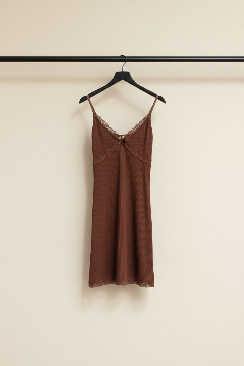 A brown ribbed camisole slip dress with lace trim along the neckline and hem, hanging on a wooden hanger against a white fabric backdrop.