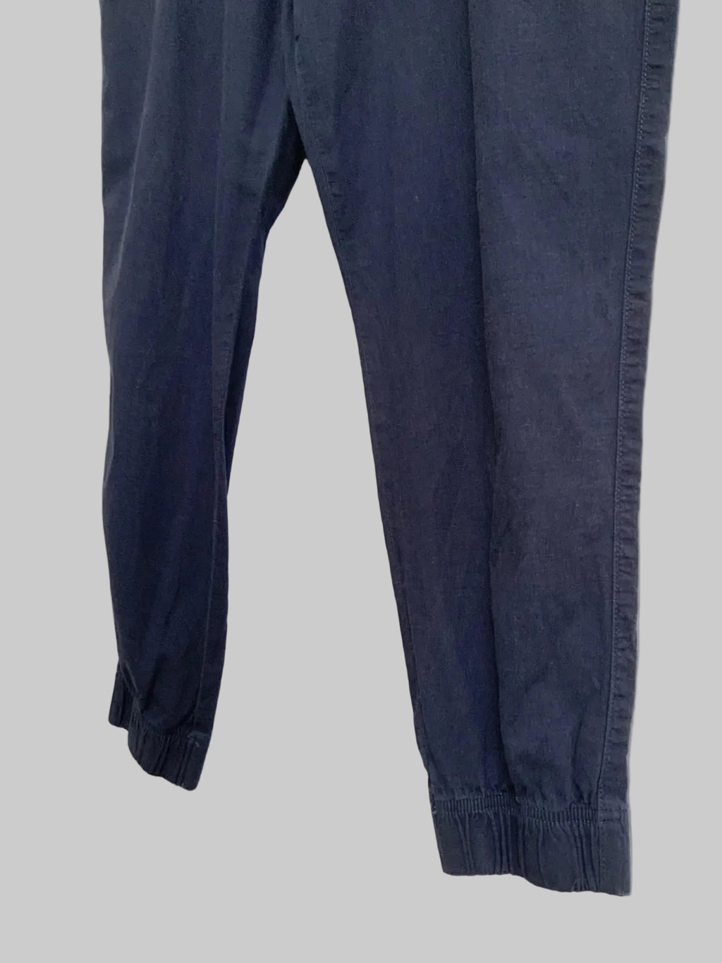 Dark navy blue pants with elastic cuffs, laid flat on a white fabric background.