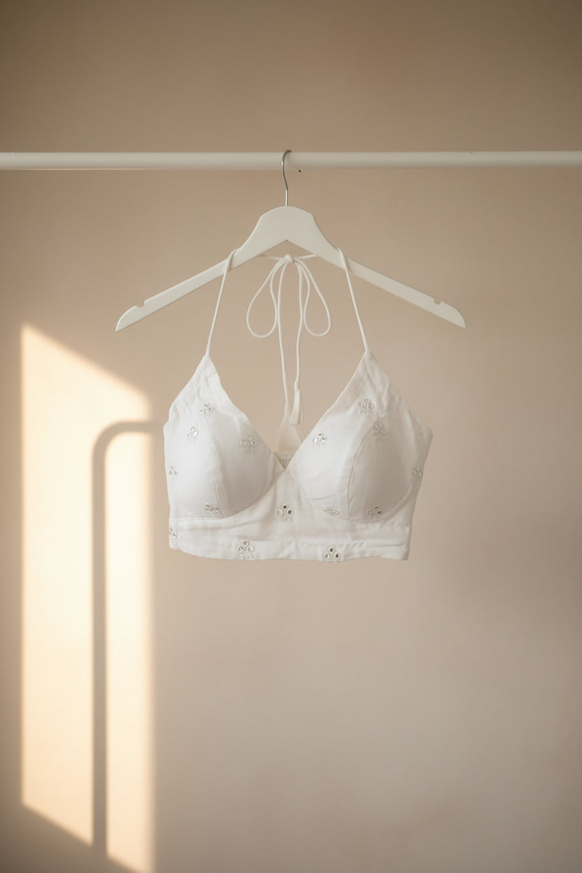 White bralette with small silver floral embellishments and a matching white underwire, laid flat on a dark brown wooden surface.