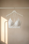 White bralette with small silver floral embellishments and a matching white underwire, laid flat on a dark brown wooden surface.