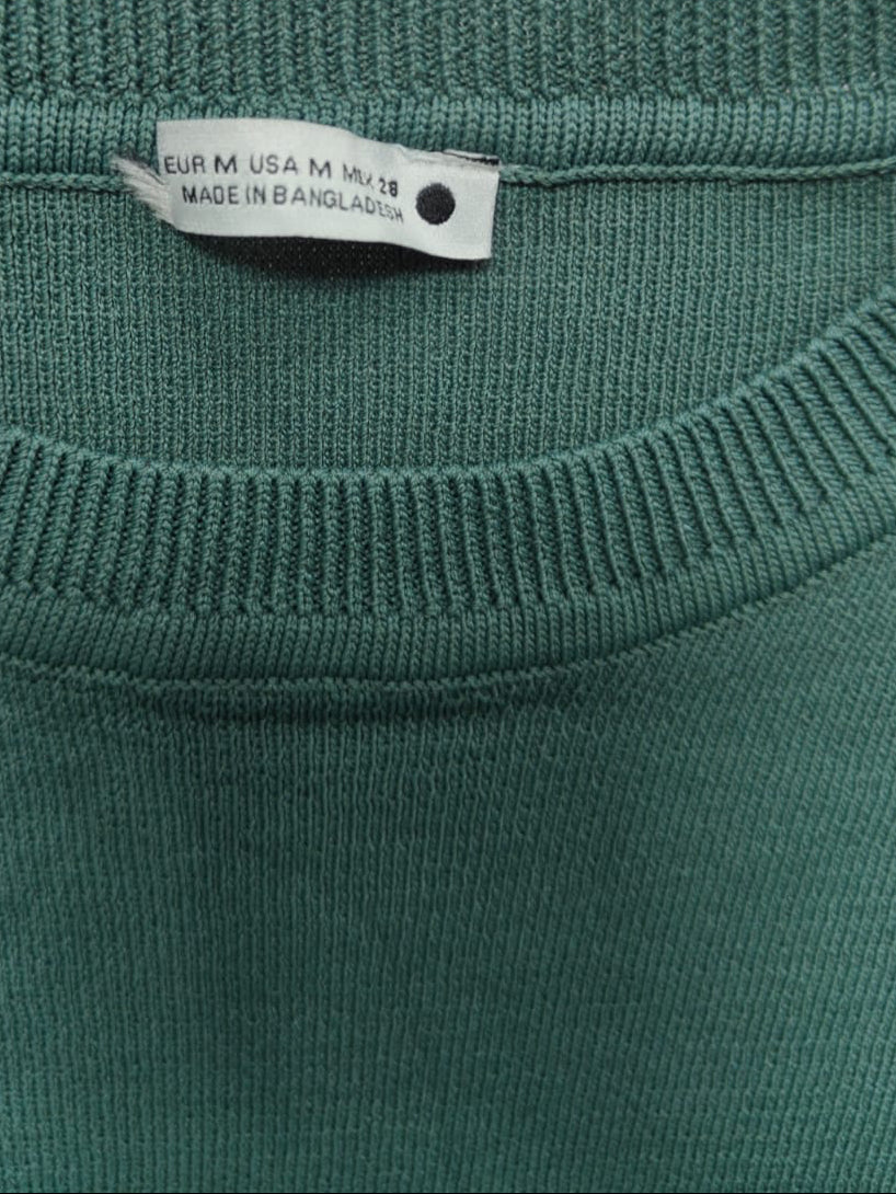 Close-up of a dark green crewneck sweater showing the inner neck label which reads 'EUR M USA M XL-XXL MADE IN BANGLADESH'.
