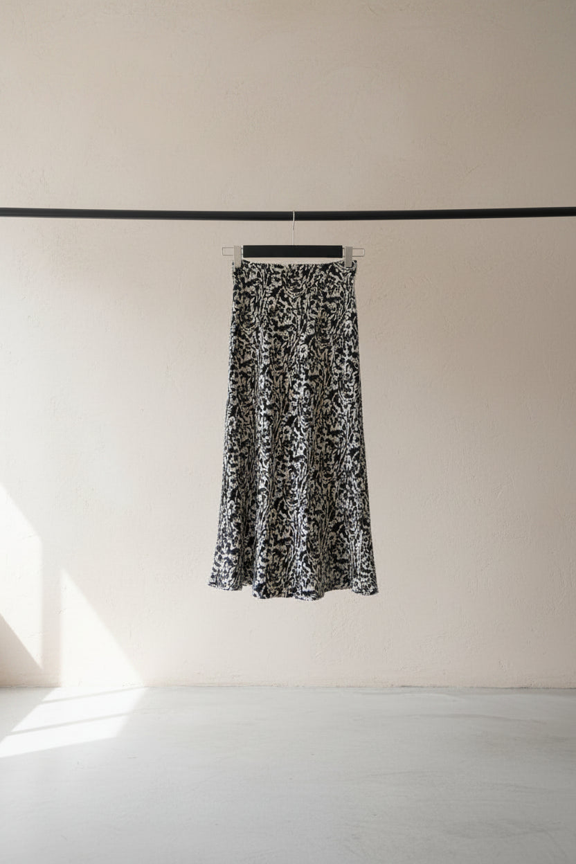 A black and white animal print midi skirt hanging from a wooden clothesline in an outdoor courtyard with potted plants and a white wall in the background.