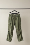 Olive green cargo pants with side flap pockets and elasticized cuffs, hanging against a gray textured backdrop.