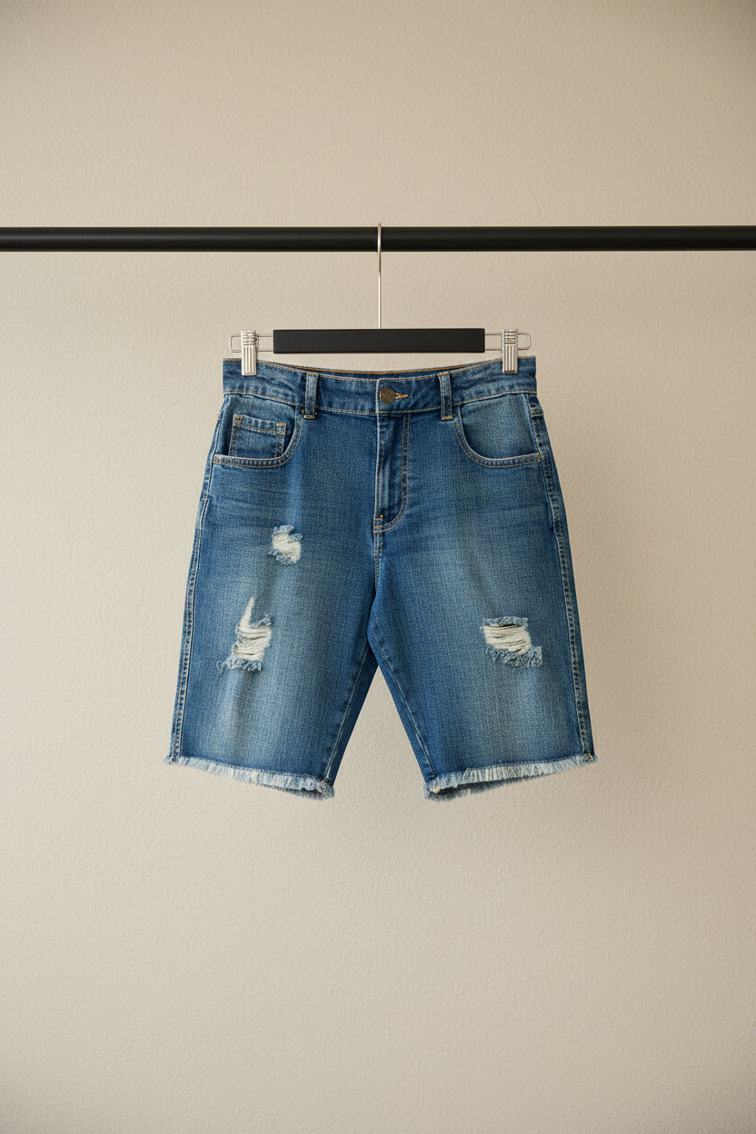 Light blue distressed denim shorts with frayed hems and ripped details, hanging on a wooden hanger against a red background.