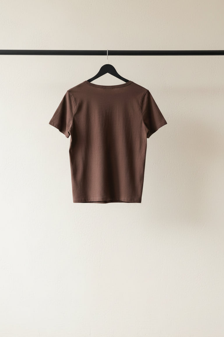 A brown short-sleeve crewneck t-shirt hanging on a wooden hanger outdoors.