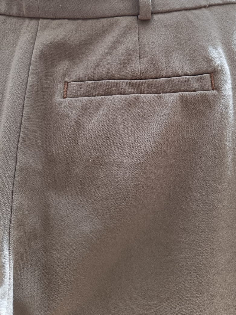 Close-up of the back waistband and pocket area of taupe brown trousers hanging on a wooden hanger.