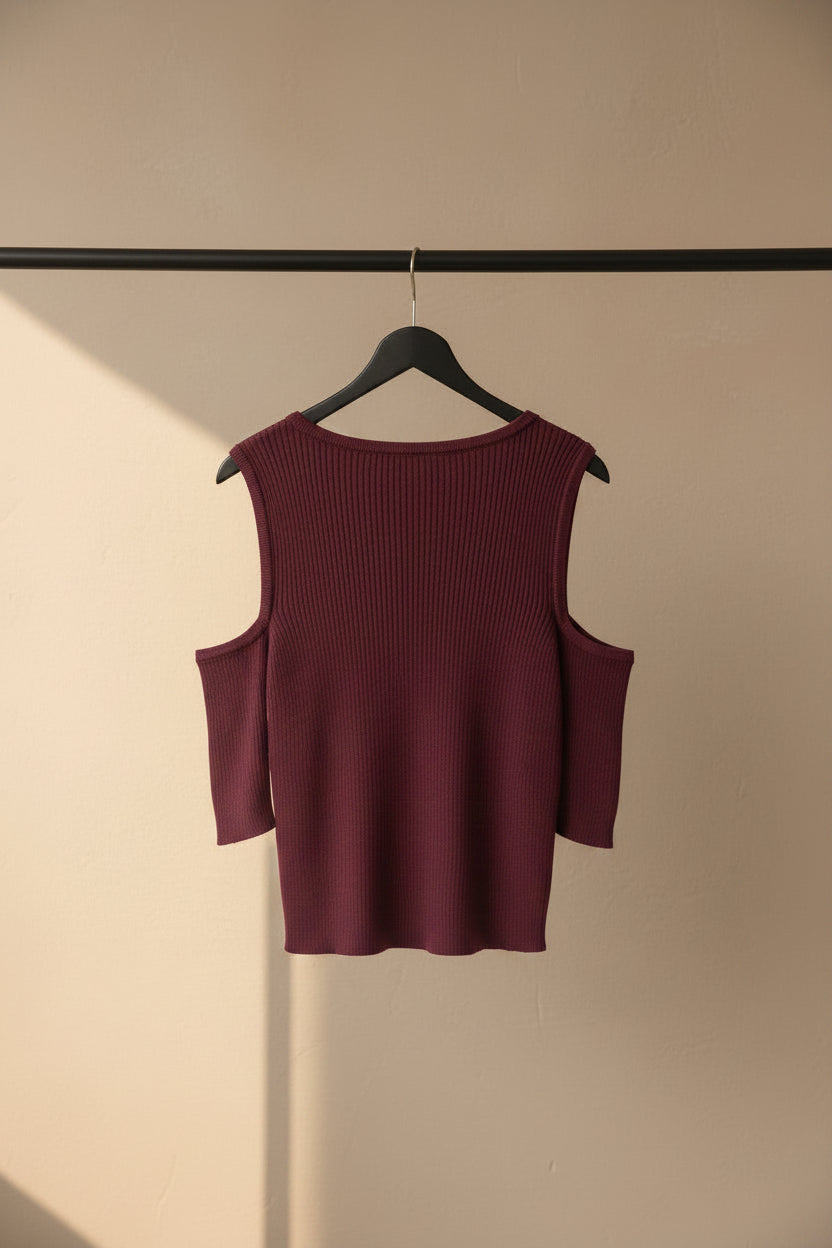 A ribbed knit cold-shoulder sweater in a deep burgundy or maroon color, laid flat on a light off-white background.