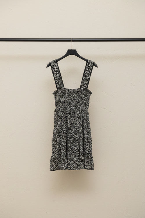A sleeveless black and white floral print dress with a ruffled neckline and tie detail at the side, laid flat on a white background.