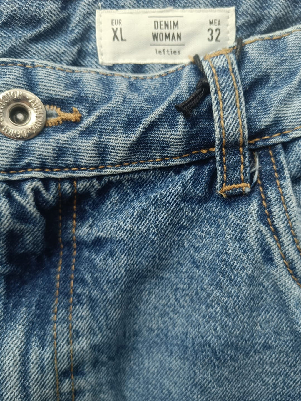 Close-up of blue denim jeans showing the waistband, size label reading XL, button, belt loop, and stitching.
