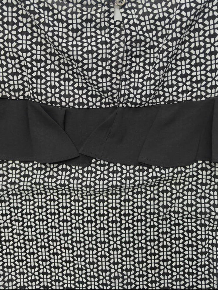 Close-up of a black and white patterned top with a solid black ruffle band across the chest.