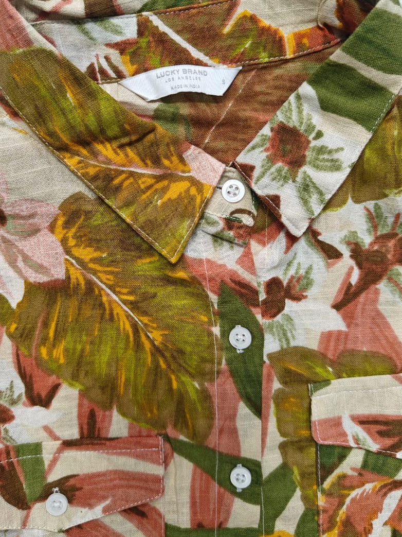 A close-up of a button-down shirt featuring a vintage tropical leaf and floral print in olive green, terracotta, mustard yellow, and cream.