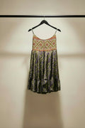 A sleeveless scoop-neck dress with a colorful geometric patterned bodice and a purple and yellow paisley print skirt, hanging on a wooden hanger 