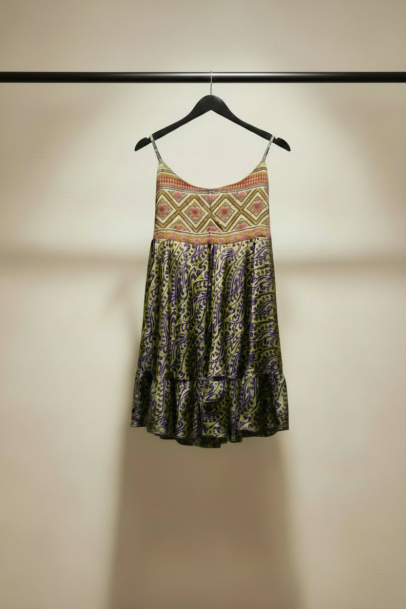 A sleeveless scoop-neck dress with a colorful geometric patterned bodice and a purple and yellow paisley print skirt, hanging on a wooden hanger 