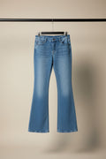 Light blue denim flare jeans hanging on a wooden hanger against a beige fabric backdrop.