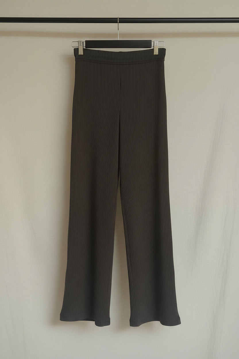 A pair of dark gray wide-leg cropped pants with a vertical ribbed texture, hanging on a wooden hanger against a white fabric backdrop.