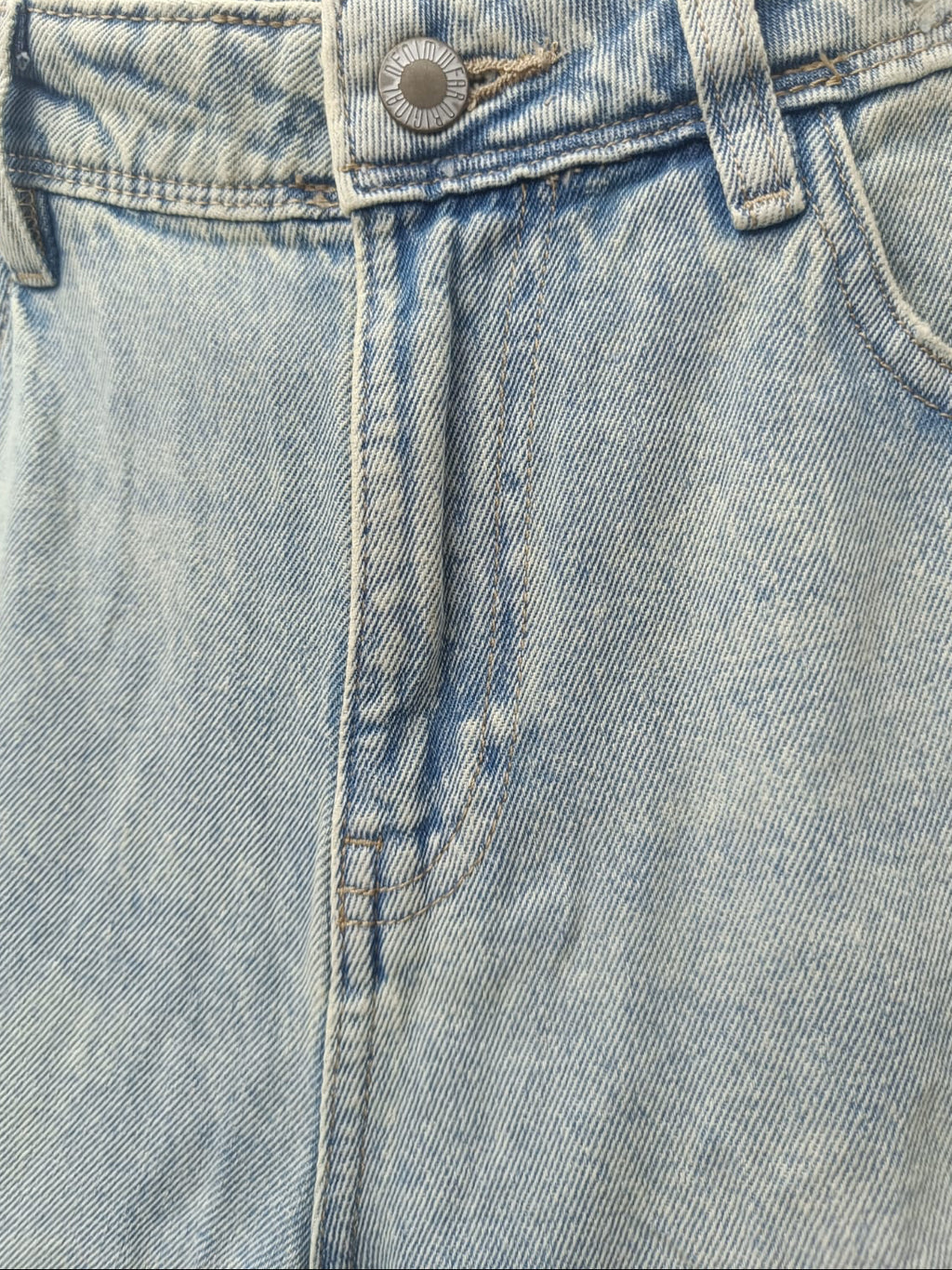 Close-up of a pair of light-wash blue denim jeans showing the waistband, button closure, belt loops, front seam, and part of the pocket area.