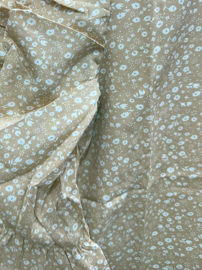 Close-up of a beige blouse with a small white floral print and a prominent ruffled sleeve, set against a dark red background.