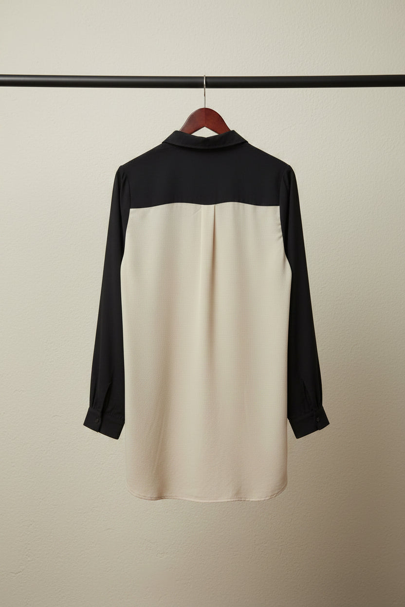 A long-sleeve colorblock shirt laid flat on a white fabric background, featuring a black yoke and black sleeves with a large cream-colored body.