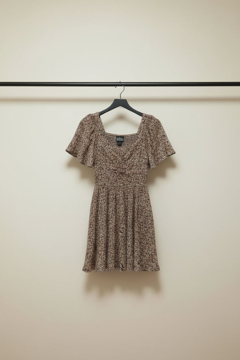 A short-sleeve mini dress with a dense small floral print in brown, beige, and muted pink tones, laid flat on a light gray background.