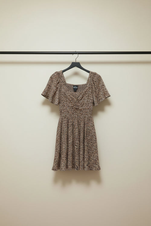A short-sleeve mini dress with a dense small floral print in brown, beige, and muted pink tones, laid flat on a light gray background.