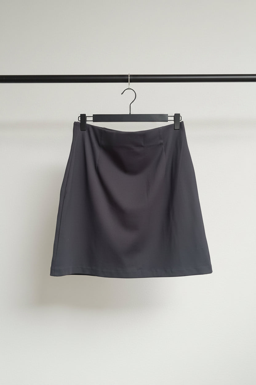 A dark gray A-line mini skirt hanging from a wooden hanger with metal clips against a white fabric background.