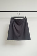 A dark gray A-line mini skirt hanging from a wooden hanger with metal clips against a white fabric background.