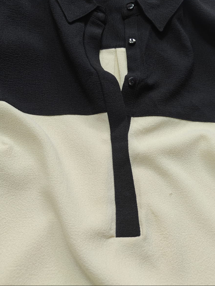 A close-up of a color-block knit polo shirt by Lee Perry, featuring a black yoke and collar with an off-white lower body and placket.
