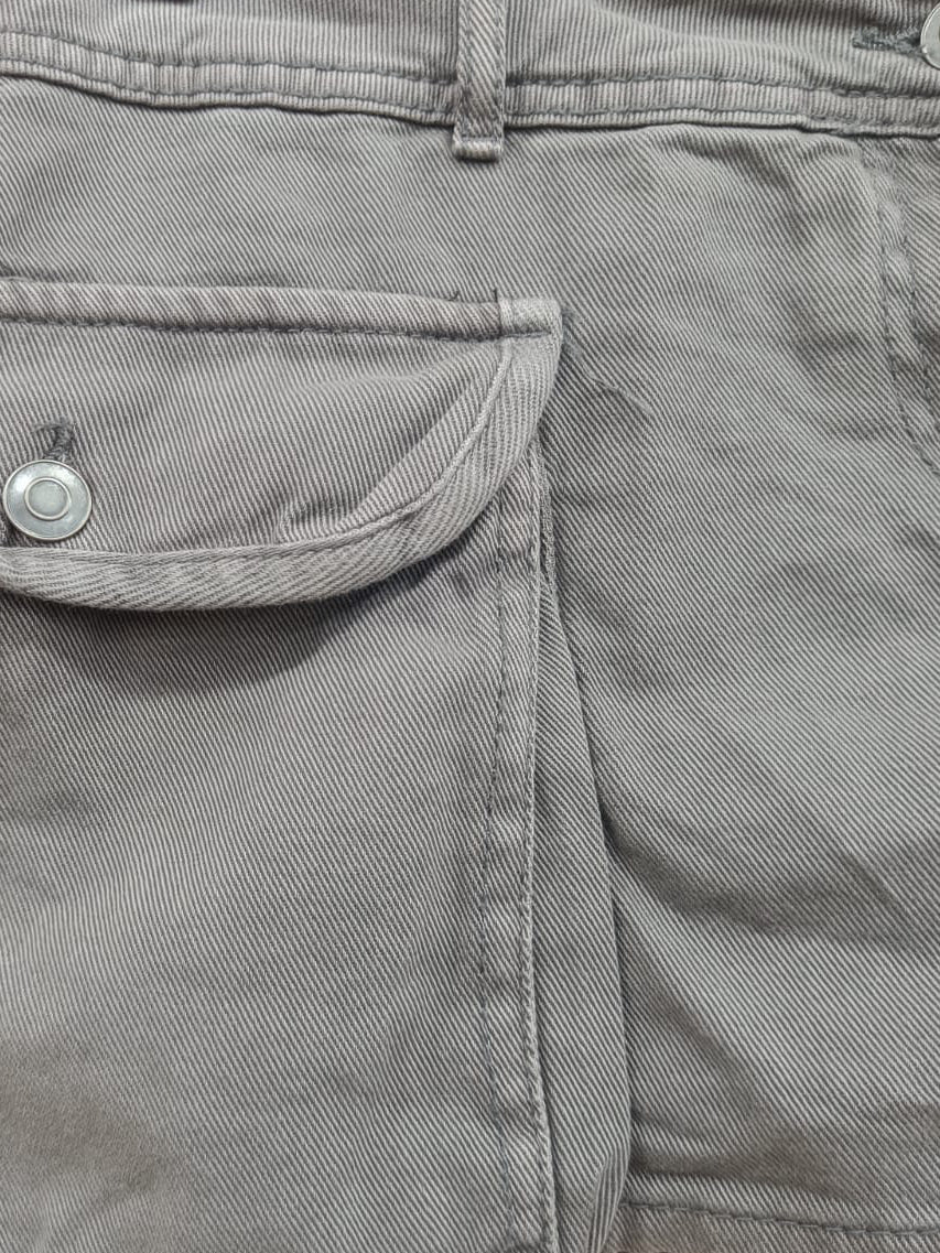 Gray corduroy shorts with a buttoned flap pocket, shown hanging on a metal hanger against a red background.