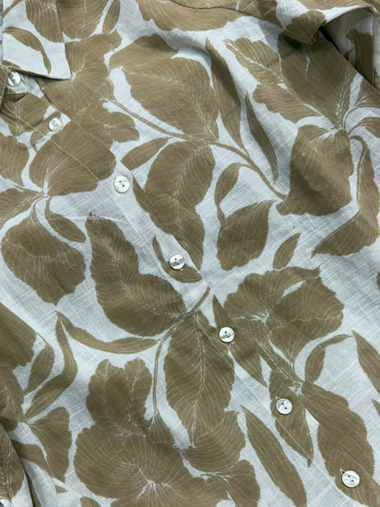 A long-sleeve button-up shirt with a brown and white leaf pattern, laid flat on a dark red background.