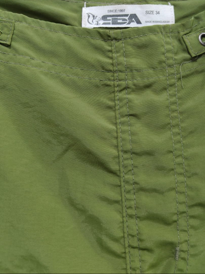 Close-up of olive green shorts showing the waistband, stitching, a white size label reading S/24, and a gray drawcord loop.