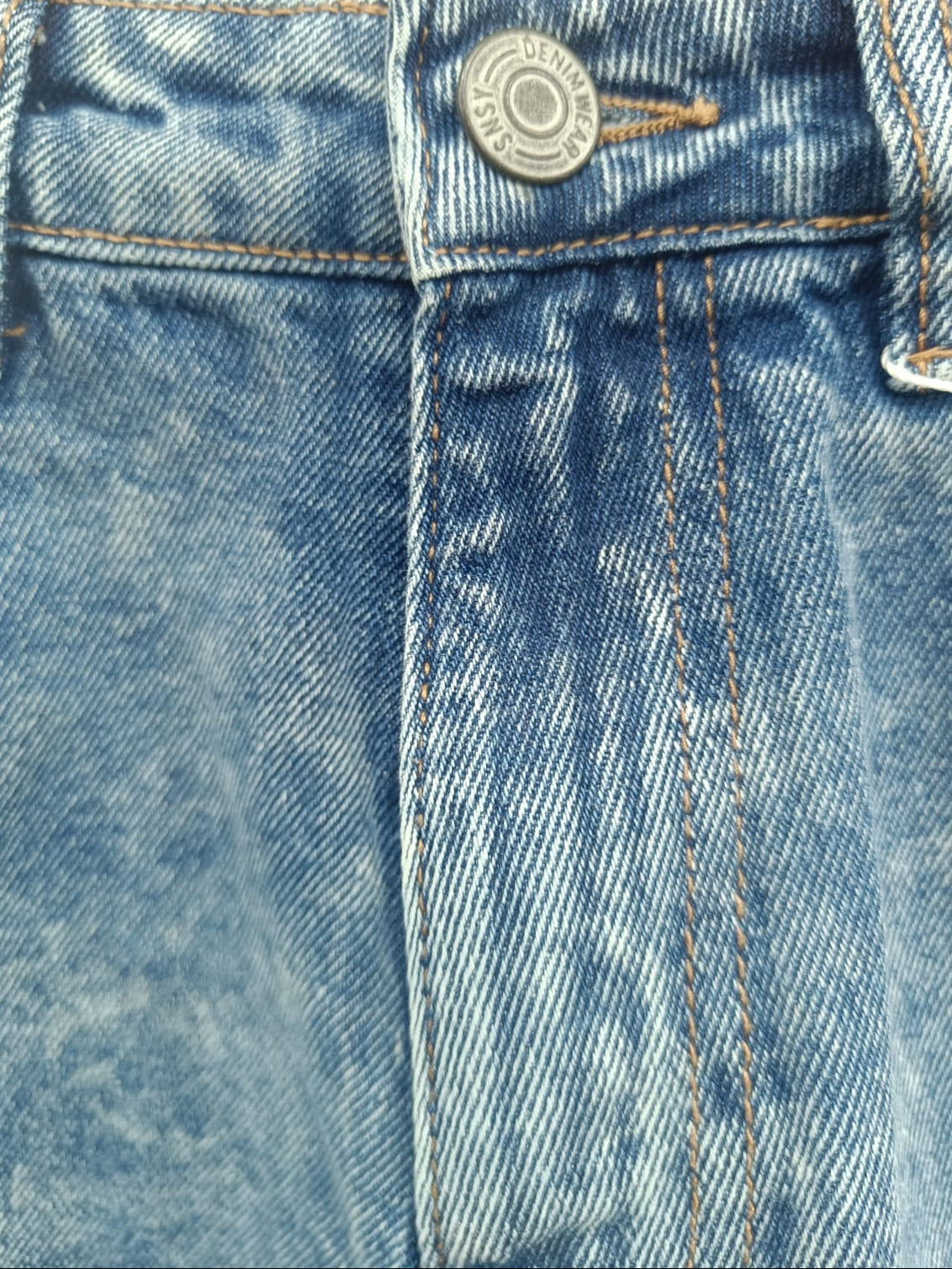Close-up of a pair of light blue denim jeans showing the waistband, button closure, belt loops, and front seam stitching.