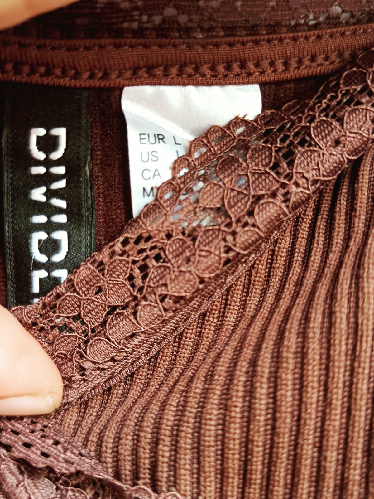 Close-up of a brown ribbed knit garment with a matching lace trim, showing a black brand label that reads DIVICE and a white size tag.