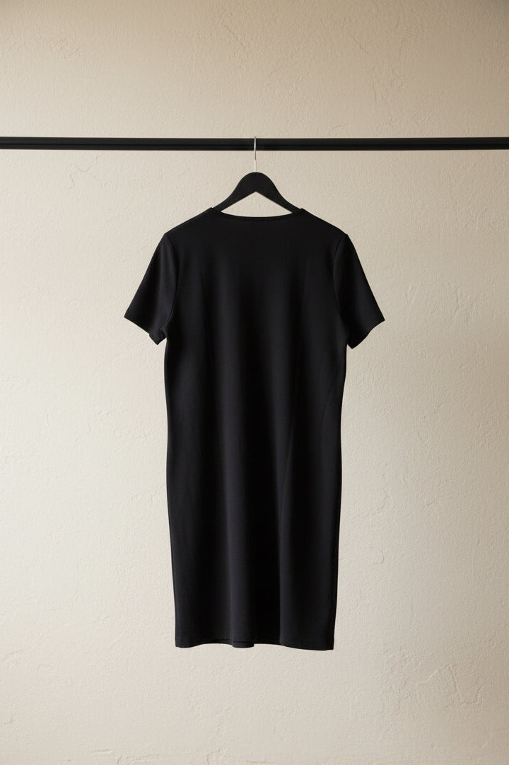 A black short-sleeve t-shirt dress hanging on a wooden hanger against a wrinkled white fabric backdrop.