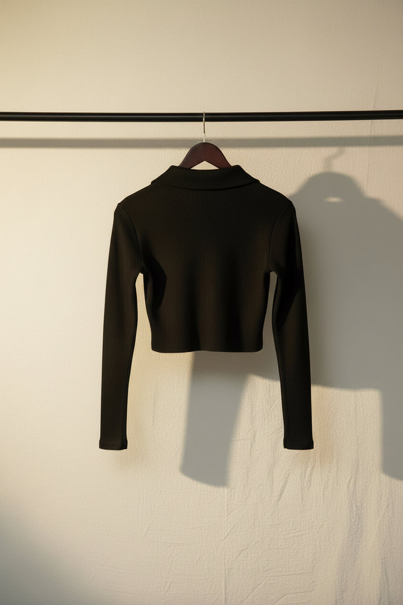 A black long-sleeve crop top with a mock neck, shown from the back on a wooden hanger against a light gray background.