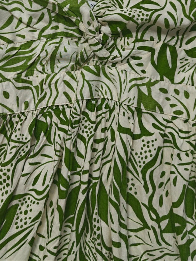 A sleeveless halter dress with a green and off-white botanical leaf pattern, featuring a gathered waist and tie-front detail.