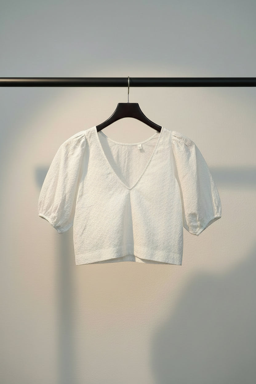 A white short-sleeve blouse with puff sleeves and a scoop neckline, laid flat on a solid red background.