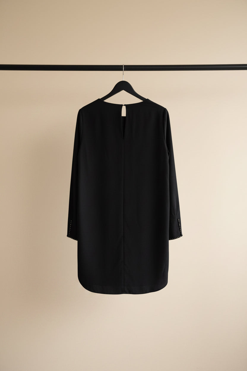 A black long-sleeve tunic dress hanging on a wooden hanger against a white fabric backdrop.