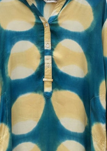 A long-sleeve V-neck top with a large abstract organic spot pattern in mustard yellow and teal blue, featuring a buttoned placket and a visible 'Aurora' brand label at the collar.