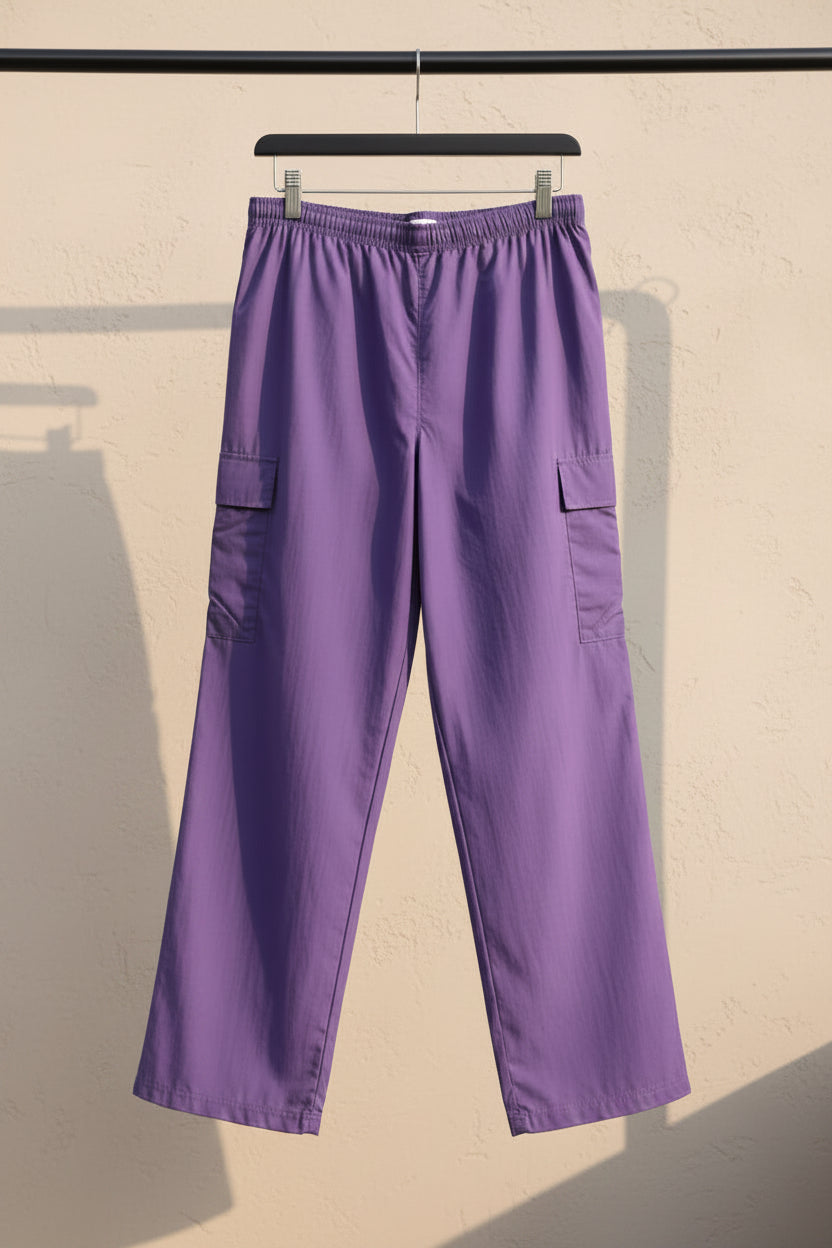 Purple cargo pants with side flap pockets, hanging against a light gray fabric backdrop.
